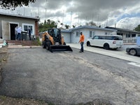 two men are working on a driveway in front of a house