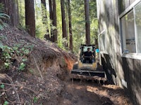 a bulldozer is parked in a wooded area near a house