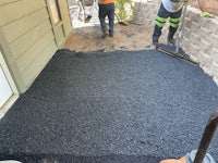 two men are working on a black paved driveway